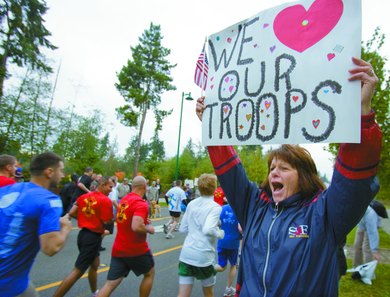 woman holding a we love our troops sign while people are running a race