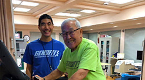 An elderly Veteran on an exercise machine assisted by a VA employee