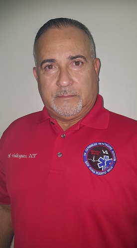 Man with red, short-sleeve, collar shirt. The left of the man’s shirt reads, H. Velazquez, ICT. The right of the man’s shirt has a blue, red and black seal that reads, VA Caribbean Healthcare System and San Juan Puerto Rico.