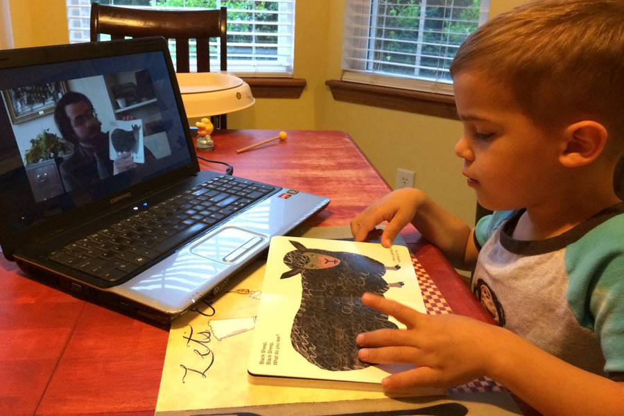 A child reading a book is guided through the book by their parent, a service member, via videophone.