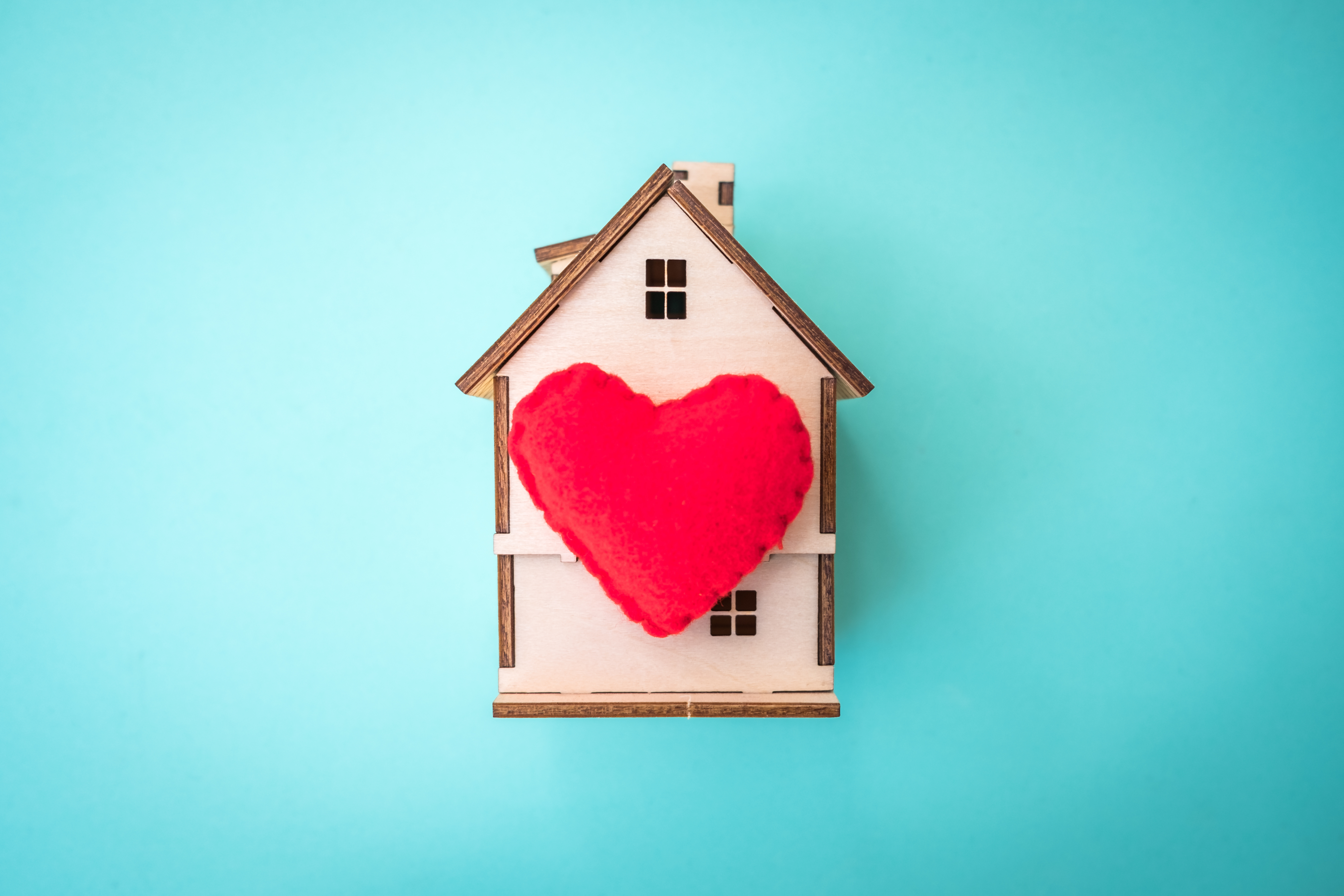 a granite teal background with a tan, wooden model of a house with a read heart in the middle.