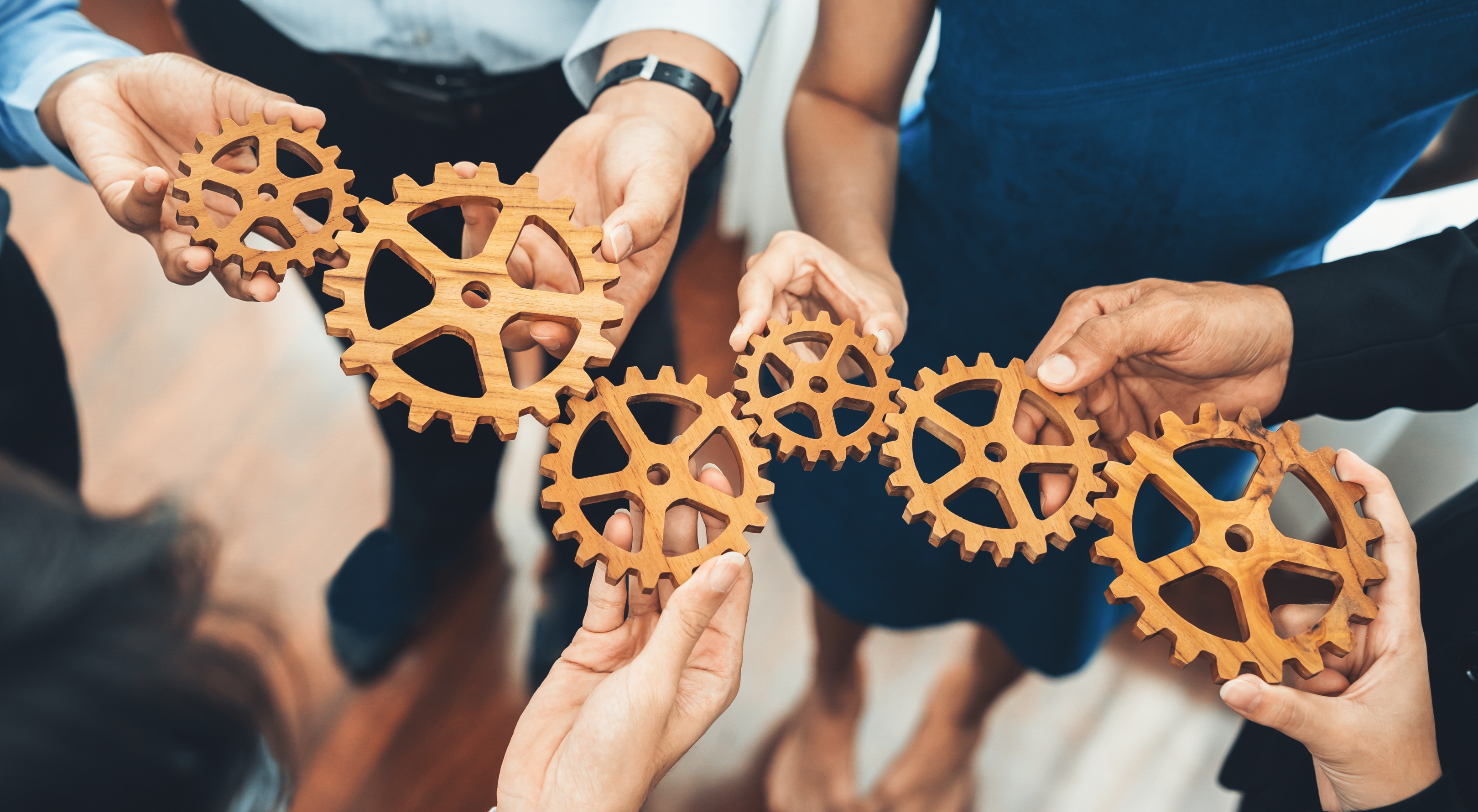 A group of people holding gears that fit together, symbolizing teamwork.