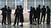 Veterans standing in a warehouse silhouetted in front of large windows.