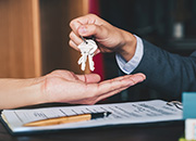 A real estate agent gives house keys to woman over a signed agreement on a table.