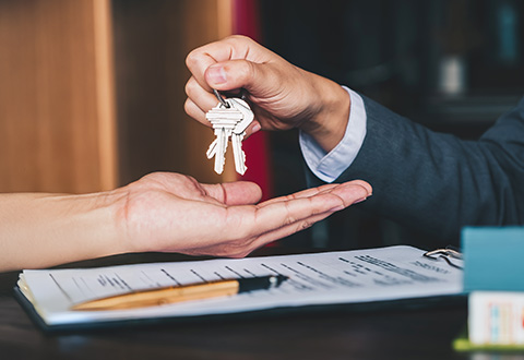 A real estate agent gives house keys to woman over a signed agreement on a table. 