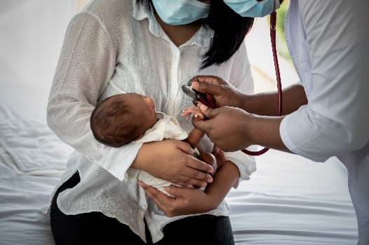 A clinician examining an infant while the infant is held by its mother.