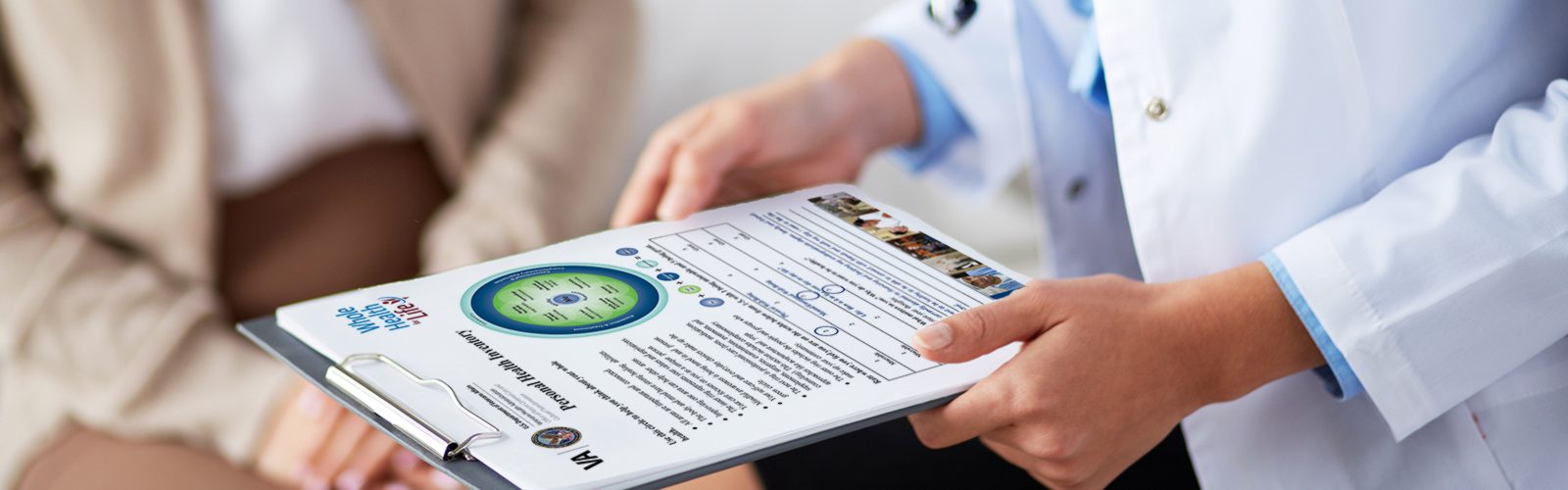 Up-close photograph of a clinician holding in both hands a patient's Personal Health Inventory on a clipboard. Patient's midsection is blurred in the background.