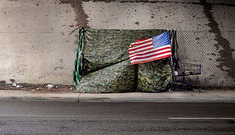 An American flag at a homeless tent made of camouflage tarp at a road underpass