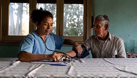 Rural doctor visiting a patient at home and taking his blood pressure - healthcare and medicine concepts